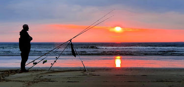 Person fishing on a beach at sunset with multiple rods from The Angling Hub