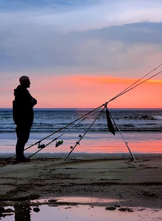 Person fishing on a beach at sunset with fishing rods from the angling hub.