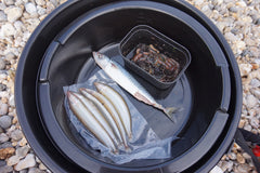 Tronixpro 27L Bait Bucket with fish and a small container of food on a gravel surface