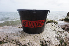 Tronixpro 27L Bait Bucket With Tray And Lid with 'TRONIXPRO' logo on a rock by the sea