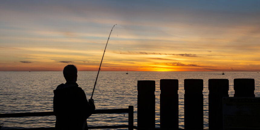 A silhouetted fisherman at the end of Redondo beach pier at sunset